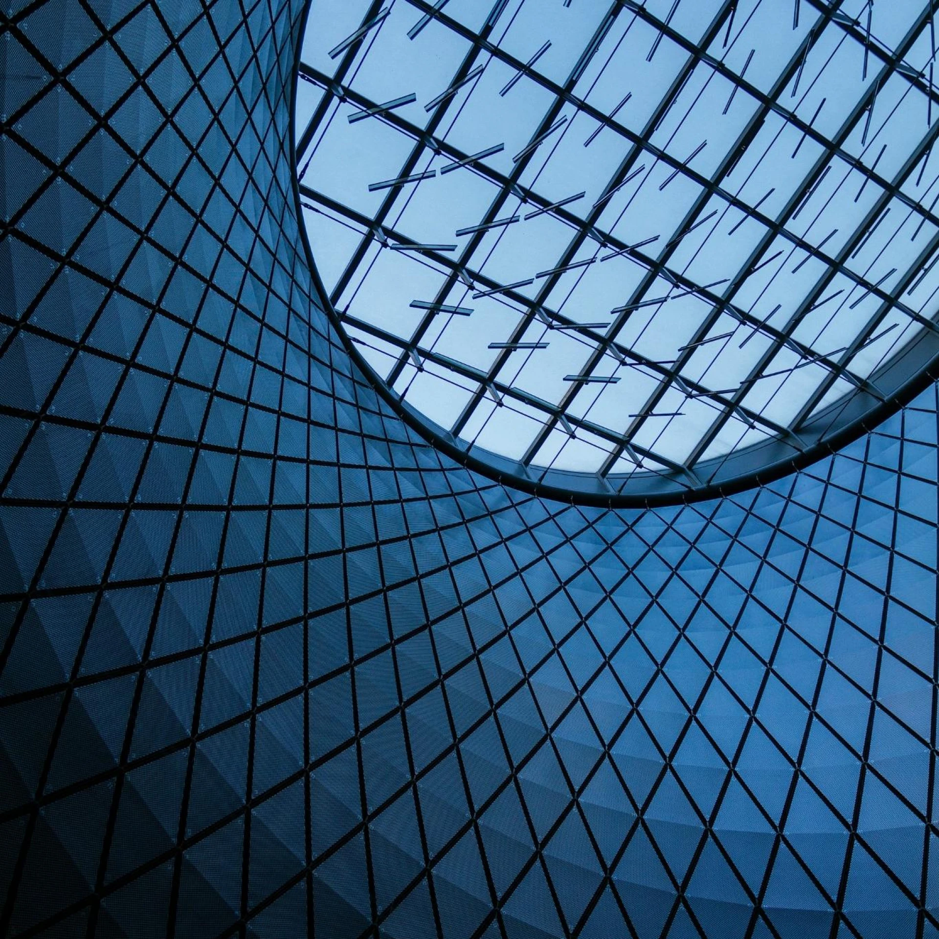 Blue-tinted interior of a building with a circular skylight, featuring a grid-like structure of intersecting lines.