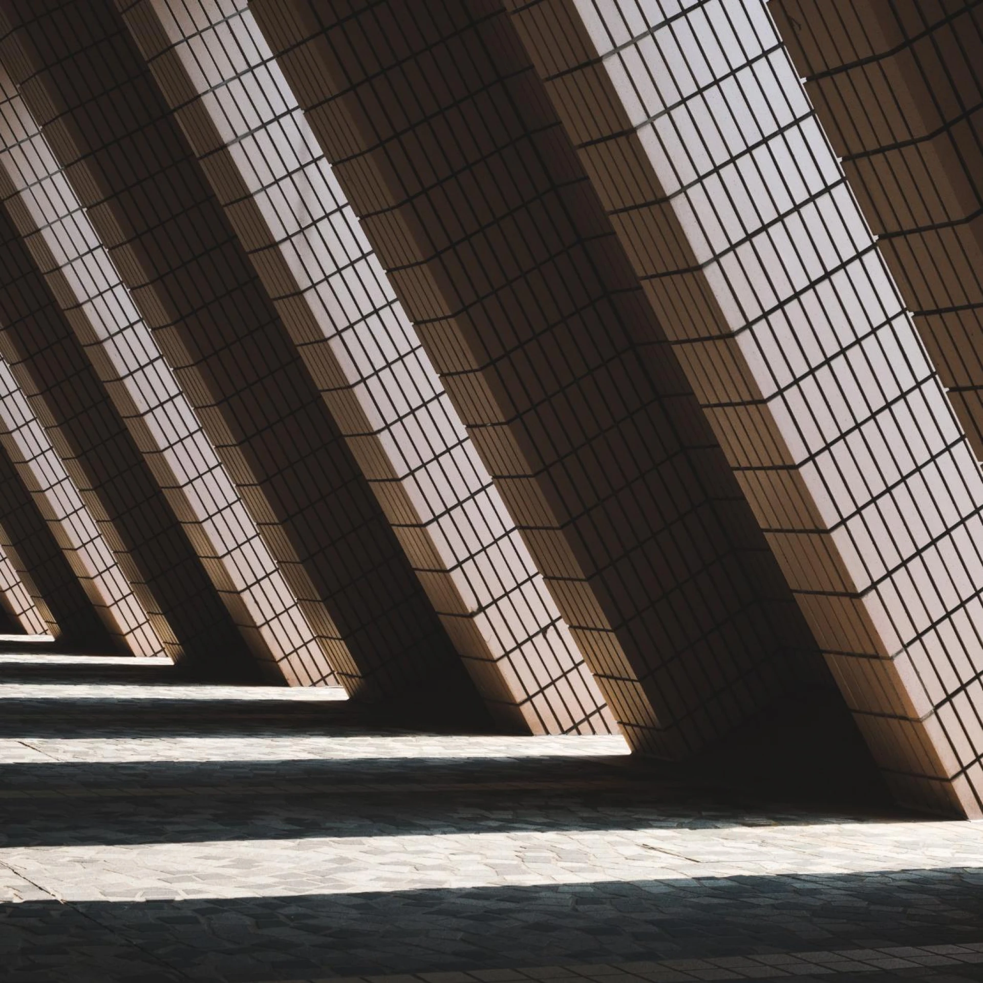 A series of angled columns casting dramatic shadows across a textured floor, creating a geometric pattern with strong contrast between light and dark.