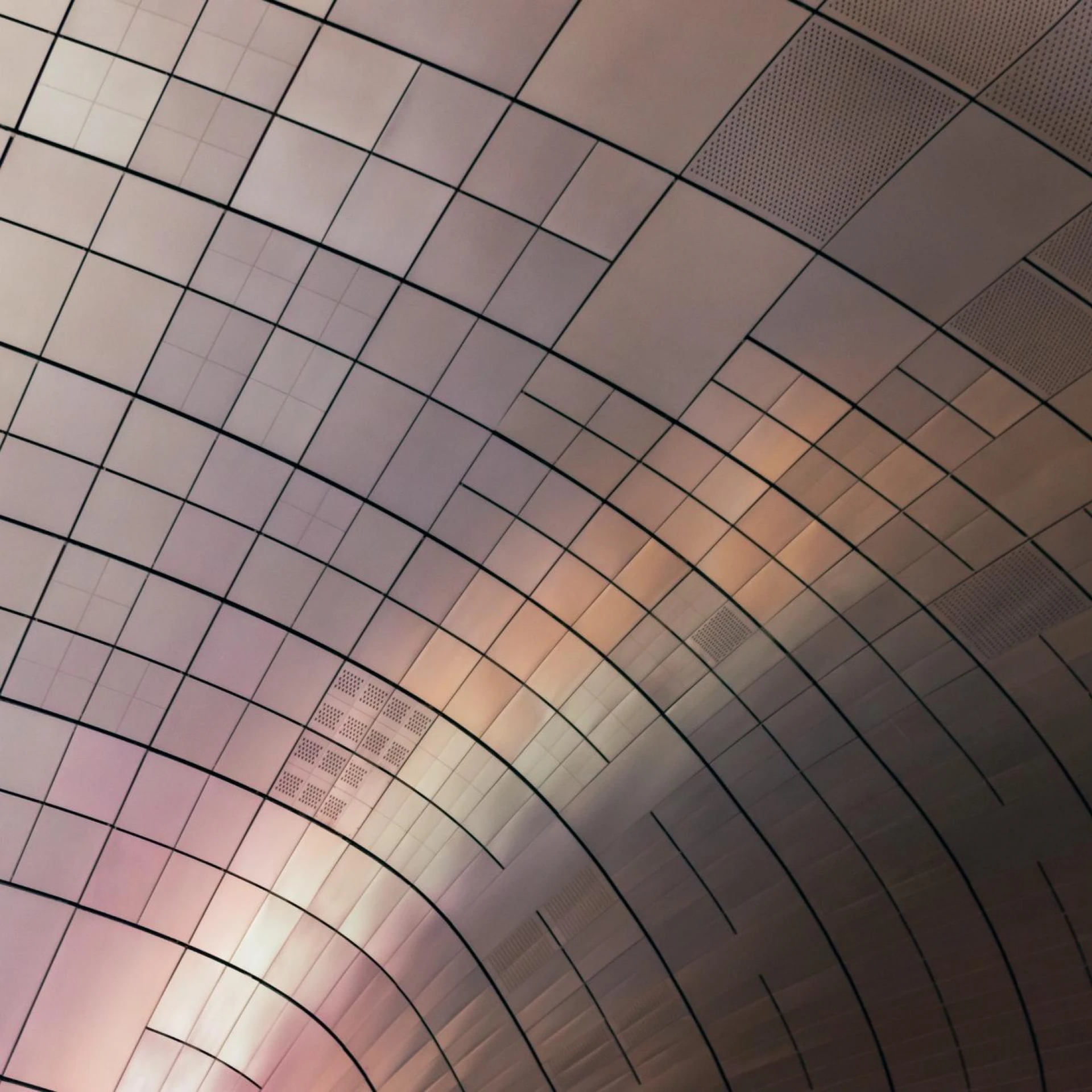 An abstract view of a curved ceiling with grid-like panels reflecting soft, gradient lighting. The design highlights modern architecture and innovative aesthetics.