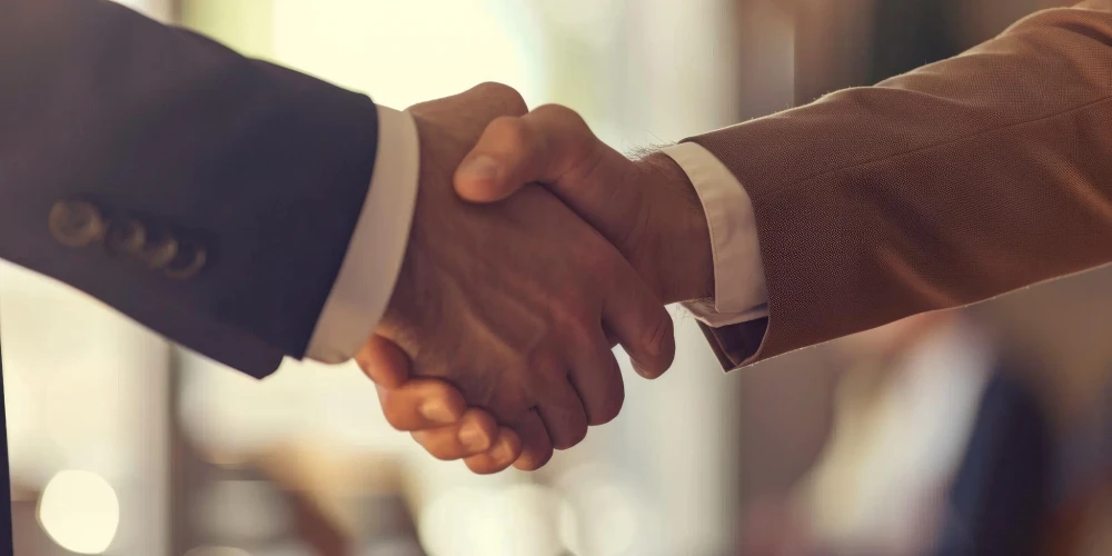 A close-up of two individuals shaking hands, symbolizing partnership and agreement, set against a softly blurred background of a professional setting.