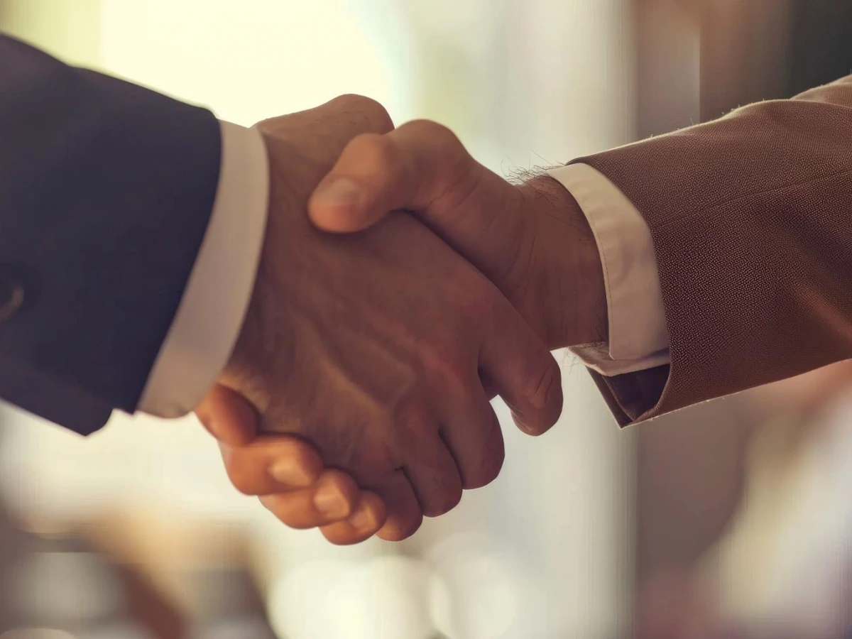A close-up of two individuals shaking hands, symbolizing partnership and agreement, set against a softly blurred background of a professional setting.